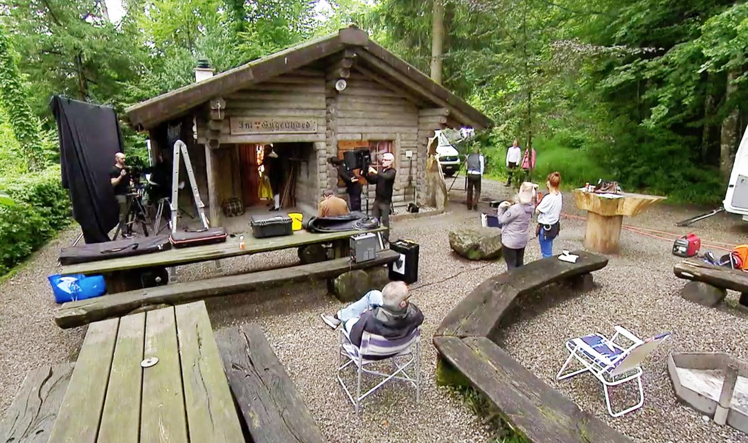 Eine Hütte am Waldrand, um welche verschiedenes Kameraequipment aufgebaut ist