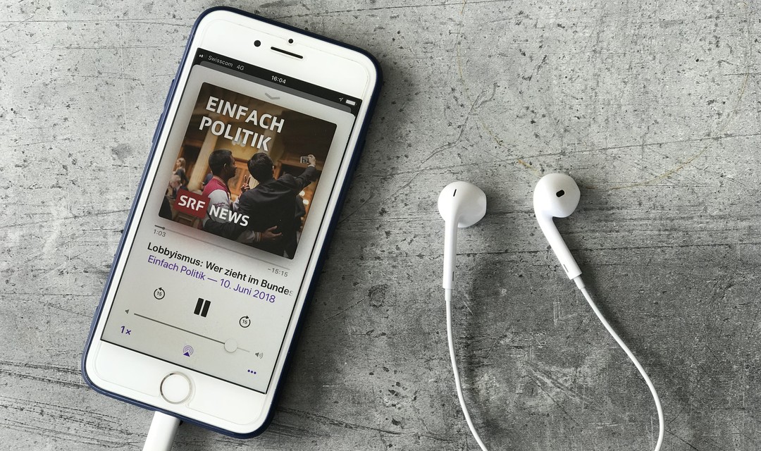 Mobiltelefon mit Podcast-App auf der «Einfach Politik» läuft, daneben Kopfhörer