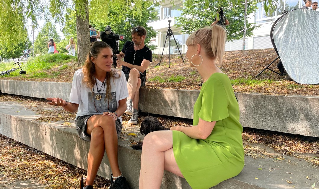 Lea Spirig spricht mit Model Tamy Glauser auf einer Treppenstufe, ein Kameramann filmt das Gespräch.