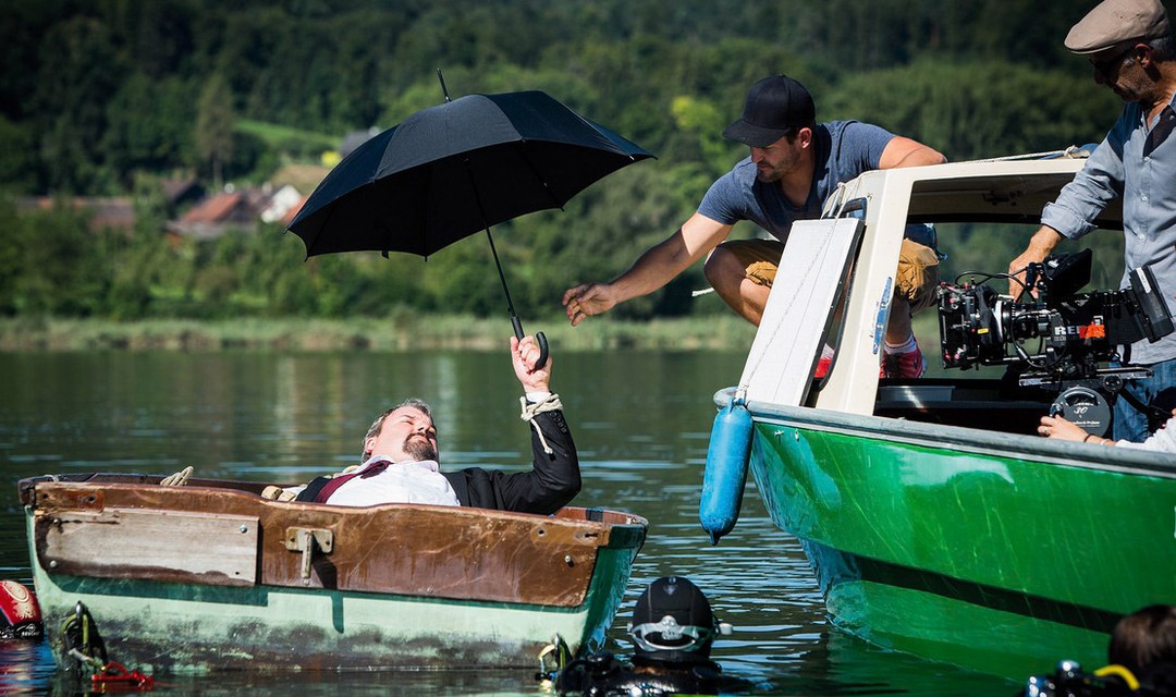 Set von «Der Bestatter». Mike Müller liegt in einem Boot im Wasser, hält dabei einen Schirm.