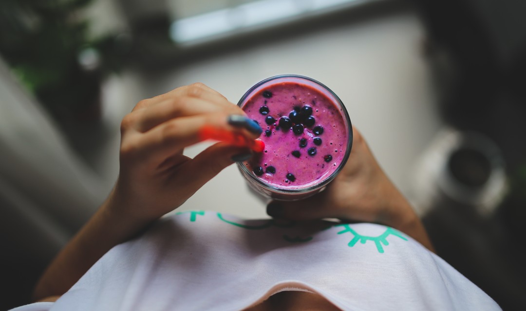 Frau hält Blaubeer-Smoothie von oben fotografiert