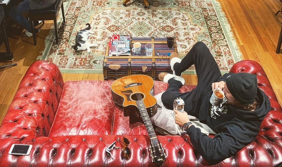 Bastian Baker sitzt im Wohnzimmer auf dem Sofa, neben ihm liegt eine Gitarre