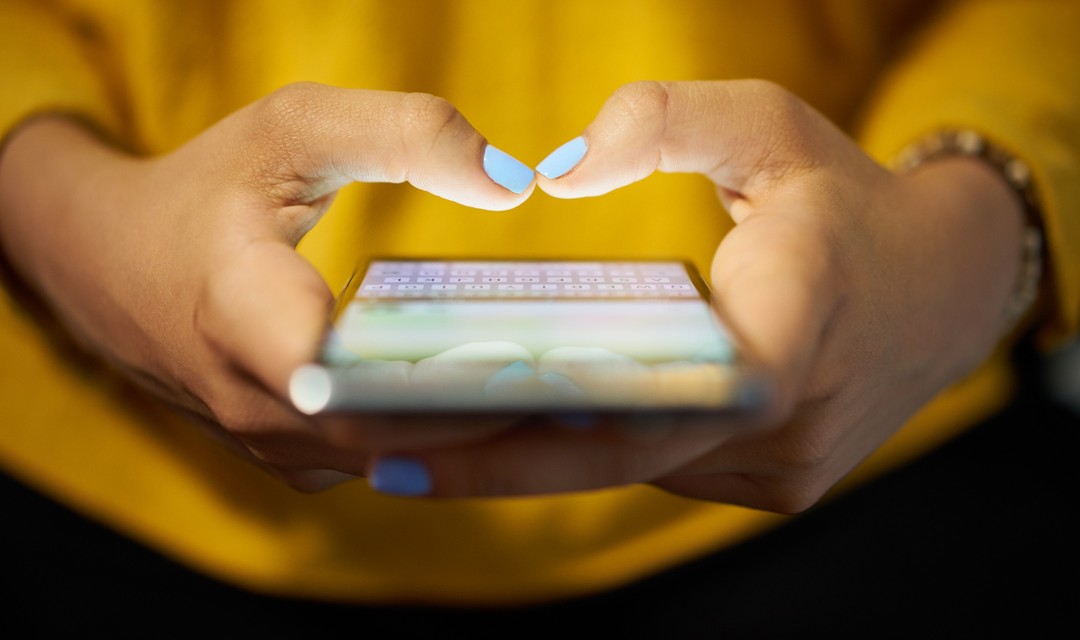 Eine Frau mit bunt lackierten Nägeln tippt auf einem Smartphone rum